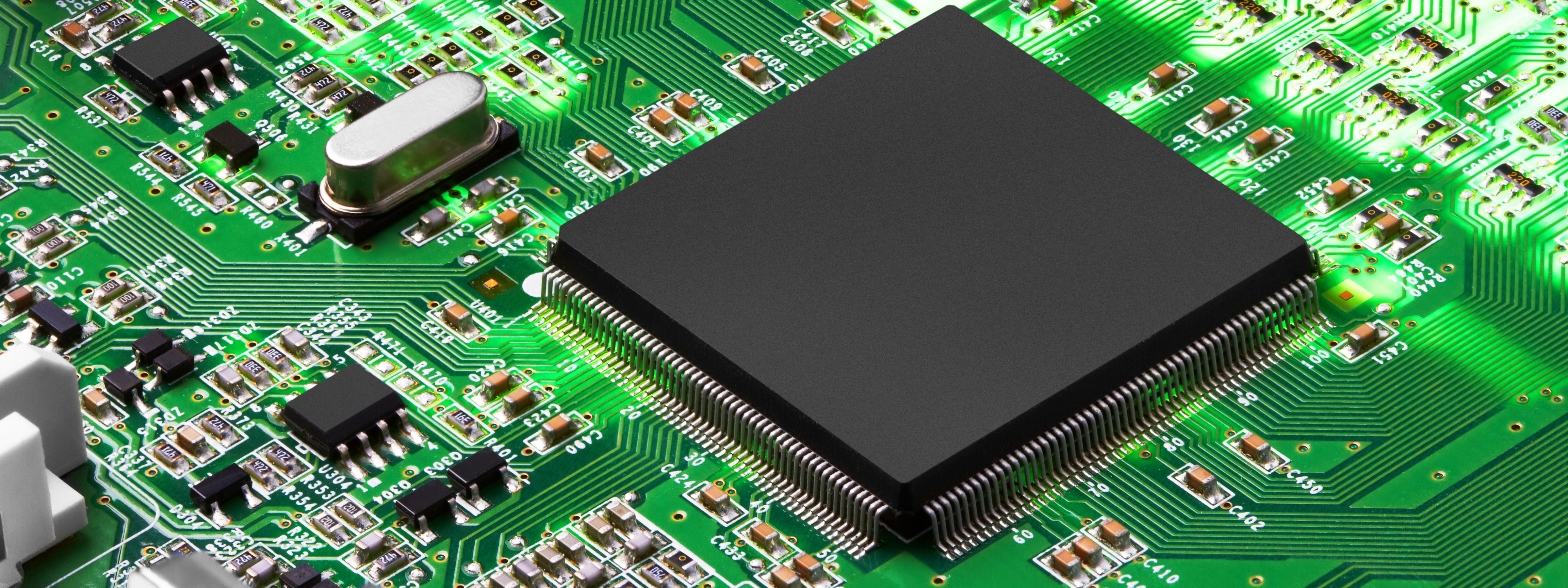 Packaged integrated circuit mounted on a printed circuit board with visible leads and surrounding surface-mount components, representing a traditional 2D semiconductor package